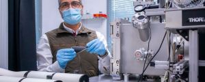 Ángel Pérez stands with a sample of a hybrid electrode in front of a laser installed in a lab.