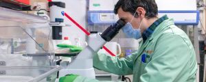 Eduardo Pérez del Río looking into a microscope in an ICMAB Lab, wearing a labcoat and latex gloves